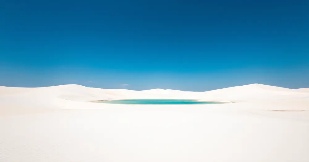 Dunas de areia branca com lagoa de água cristalina entre elas sob céu azul